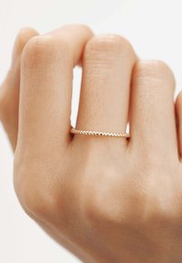 Anillo de oro con una banda lisa y texturizada descansando sobre una mano de piel clara, que presenta un fino diseño de cuentas alrededor de la circunferencia.