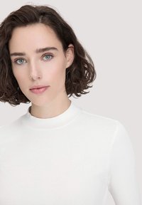 Weißes, geripptes Turtleneck-Oberteil mit glatter Textur, figurbetontem Schnitt und hohem Halsausschnitt. Hat lange Ärmel und saubere Nähte.
