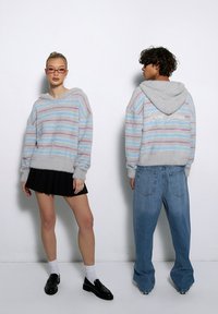 Pasiaste sweter z kapturem z miękkiego, puszystego materiału w jasnoniebieskim, różowym i szarym kolorze. Posiada obniżone ramiona i ściągacze.