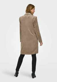 Beige kordjacka med slitskrage, långa ärmar och rak snitt. Bärs över svarta byxor och ankelstövlar, vilket framhäver den ribbade texturen.