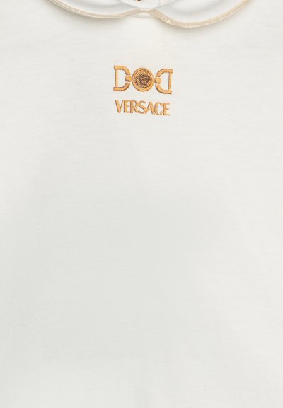 Vit bomullsskjorta med rundad krage och guldbroderad "Versace"-logotyp med en cirkulär emblem ovanför. Slät Textur.