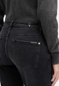 Ciemnoszare jeansy z denimu z wysokim stanem, z tylną naszywaną kieszenią i metką oznaczoną "7". Tkanina ma gładką fakturę.