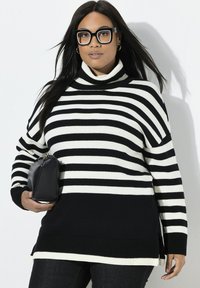 Maglione a collo alto a righe bianche e nere con orlo a coste e spacco laterale, abbinato a una piccola borsa nera.