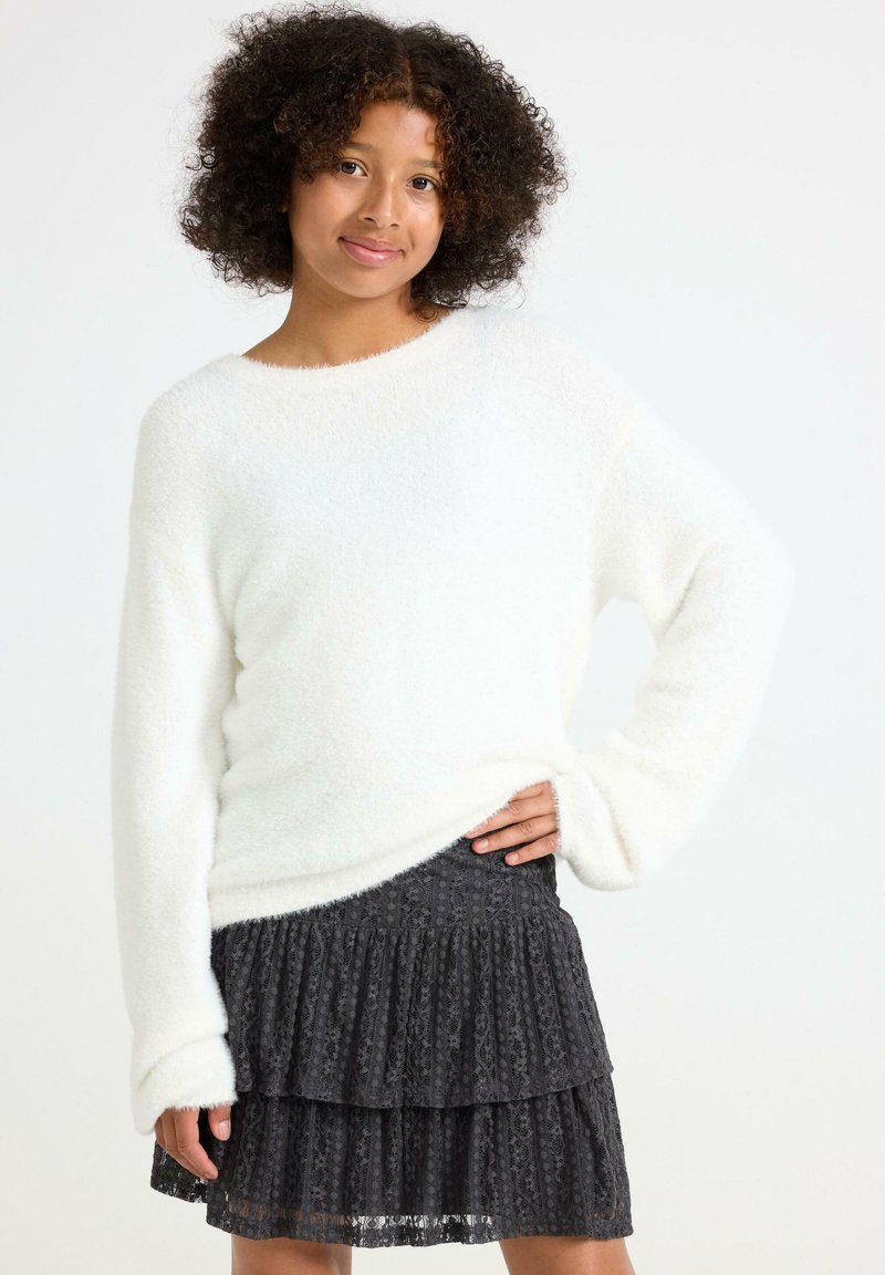 Pull en peluche blanc avec un décolleté large et des manches longues, associé à une jupe en dentelle noire plissée avec un design en couches.