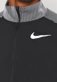 Zwarte zip-up jas met gestreepte kraag, voorzien van een wit Nike-logo op de borst. Gemaakt van soepel, lichtgewicht stof.