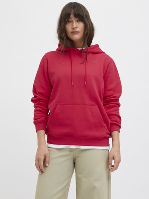 Rød hettegenser med frontlomme, designet med snorjustering, kombinert med lys beige bukser som viser en avslappet passform.