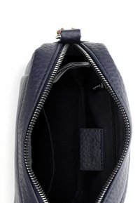 Granatowa torba ze skóry o teksturowanej powierzchni z zamkiem błyskawicznym, z gładkim wnętrzem i małą metką wewnątrz. Elementy wykończeniowe w srebrnym kolorze.