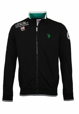 Veste noire zippée avec logo vert sur la poitrine, texte US Polo Assn. et drapeau sur l'épaule, ainsi qu'un écusson sur la manche gauche.