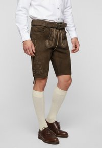 Hnědé kožené šortky s dekorativním prošitím, bočními kapsami a knoflíkovými detaily. V kombinaci se světlými podkolenkami a hnědými botami.