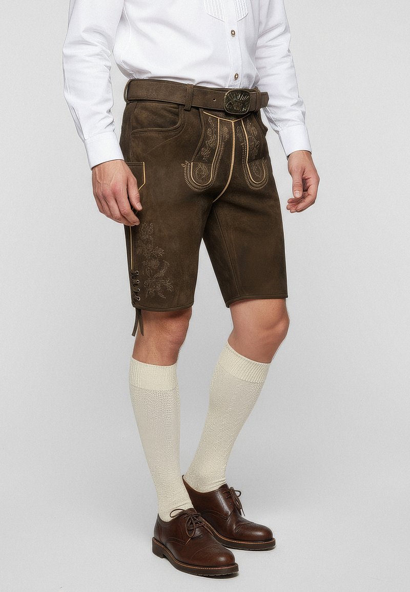 Hnědé kožené šortky s dekorativním prošitím, bočními kapsami a knoflíkovými detaily. V kombinaci se světlými podkolenkami a hnědými botami.