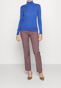 Niebieski sweter z golfem w połączeniu z brązowymi spodniami o prostych nogawkach i brązowymi wzorzystymi szpilkami, prezentujący przylegający fason o gładkiej fakturze.