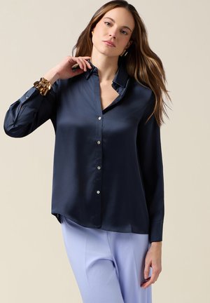 Camisa de satén azul marino con botones, mangas largas, cuello y bajos redondeados. Presenta una textura suave, cierre frontal de un solo pecho y botones tono plateado.