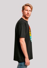 Schwarz, kurzärmliges T-Shirt mit einem bunten, abgetragenen Grafikdruck in Rot, Orange, Gelb und Aqua auf der Vorderseite. Klassische Passform, aus Baumwolle.