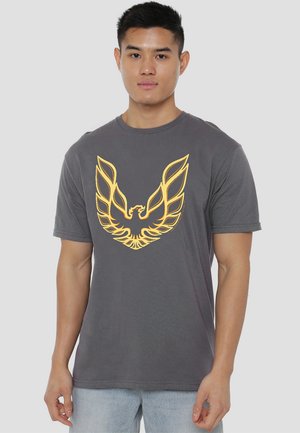 Graues Baumwoll-T-Shirt mit einem großen gelben Flügel-Emblem auf der Vorderseite. Kurze Ärmel, runder Ausschnitt, entspannte Passform. Weicher Stoff.