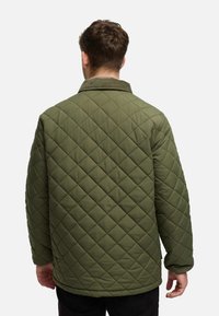 Quiltet olivengrøn jakke med en kordfløjlskrage, der har et diamantmønster og en afslappet pasform, set fra bagsiden.
