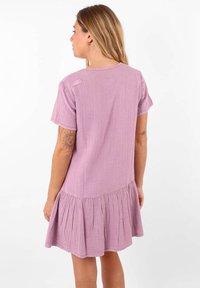 Robe lilas à manches courtes avec un tissu texturé et un ourlet évasé. Présente un design simple et une accentuation à l'épaule.