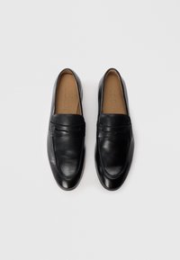 Mocassins en cuir noir avec une finition lisse, bout arrondi et couture décorative sur le devant. Intérieur rembourré, design simple, style enfiler.