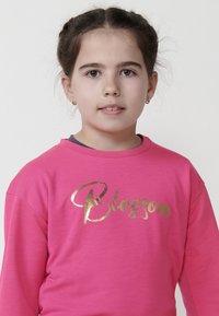 Chemise à manches longues rose avec un texte doré brillant "Blossom" sur le devant. Tissu doux avec une coupe décontractée et un col rond.