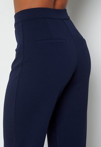 Granatowe spodnie o dopasowanym kroju, wykonane z gładkiego materiału, z wysokim stanem, tylnymi kieszeniami i eleganckim krojem, idealne na formalne okazje.