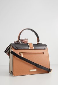 Sac à main structuré marron et noir avec une anse supérieure, une bandoulière amovible, une poche zippée avant et un foulard décoratif. Texture lisse.