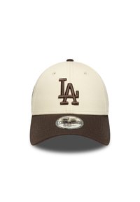 Gorra de béisbol color crema con visera marrón oscuro. Presenta un logotipo bordado en marrón de "LA" y una etiqueta ajustable redonda en la visera.