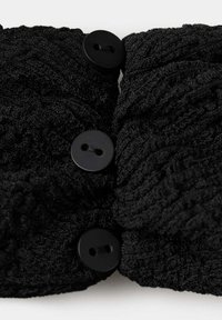 Tissu tricoté noir avec motif torsadé comportant trois boutons noirs ronds passés à travers deux trous chacun.