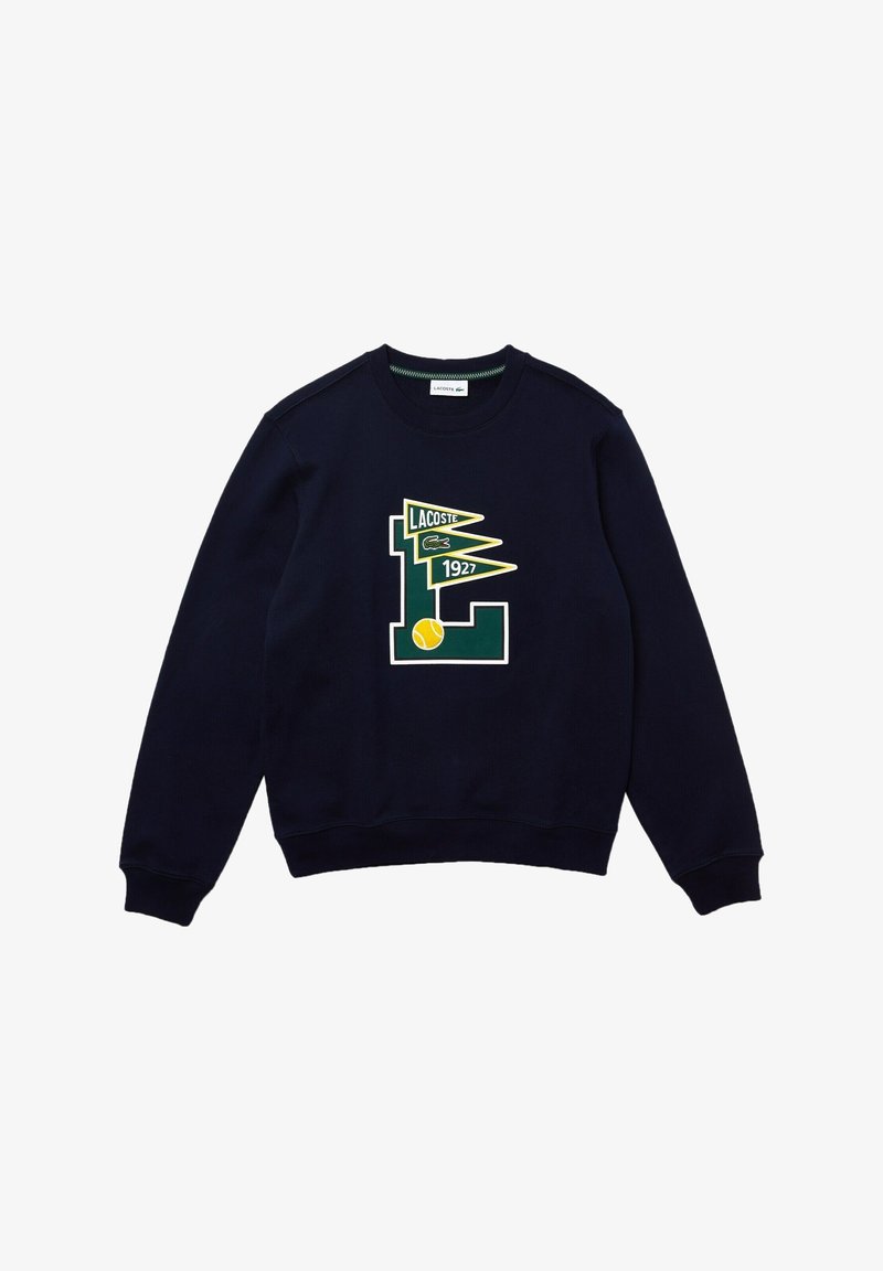 Sweat-shirt bleu marine avec un grand logo Lacoste vert et jaune, accompagné d'une balle de tennis et d'un design graphique daté de 1927. Texture de tissu douce.