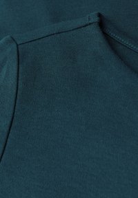 Tissu en coton teal avec une texture lisse, bénéficiant d'un col rond et de bords surpiqués. Le tissu semble doux et légèrement extensible.