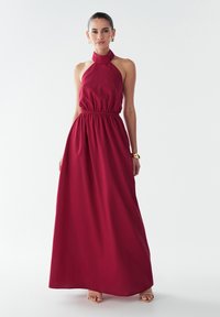 Maxikleid in Dunkelrot, aus leichtem Stoff gefertigt. Mit Neckholder, gerafftem Taillenbund und fließendem Rock. Glatte Textur, schlichtes Design.