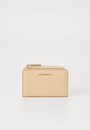 Portefeuille en cuir couleur pêche avec une finition texturée, matériel de fermeture éclair doré et logo "Coccinelle" embossé à l'avant. Design compact et rectangulaire.