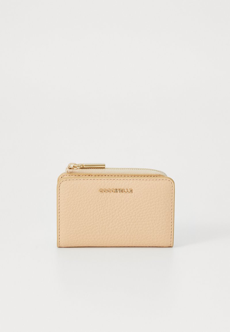 Peach-colored leather wallet with textured finish, gold zipper hardware, and embossed "Coccinelle" logo on the front. Compact rectangular design.