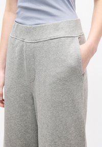 Κοντινή λήψη ενός ατόμου που φοράει ανοιχτό γκρι φόρμα με ελαστική μέση, με το ένα χέρι να βρίσκεται μέσα σε πλαϊνή τσέπη.