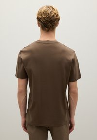 T-shirt in cotone marrone con collo rotondo, maniche corte e texture liscia. La parte posteriore è semplice, senza decorazioni.