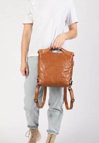 Brauner Leder-Rucksack mit glatter Textur, einem oberen Griff, verstellbaren Schultergurten und einem minimalistischen Design.