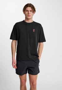 Svart bomullströja med rund halsringning och korta ärmar, med tre rosa chevronränder på vänster bröstområde.