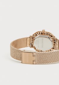 Metallic rose gold watch featuring a mesh band, octagonal case, and a clasp closure. The back displays a reflective silver surface.