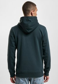 Dark green hoodie made of soft material features a drawstring hood, ribbed cuffs, and a relaxed fit. Designed with a smooth texture.