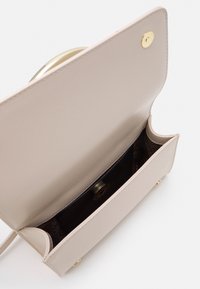 Beige läderväska med en strukturerad form, som har en guldkonfidensknapp som stängning och en kontrasterande svart inredning. Inre ficka synlig.