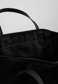 Czarna torba na ramię z zamkiem błyskawicznym, o gładkiej powierzchni, mocnych uchwytach i wewnętrznej kieszeni w kontrastowym, wzorzystym wnętrzu.