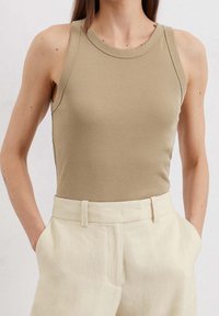 Top sin mangas de color marrón claro, hecho de una tela suave, con un escote redondeado, combinado con pantalones de tiro alto de color claro que cuentan con bolsillos laterales.