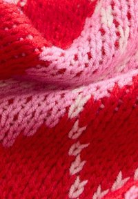 Strickstoff in verschiedenen Rottönen und Rosatönen, mit einem strukturierten Muster und helleren Akzenten, das ein geschichtetes, weiches Erscheinungsbild erzeugt.