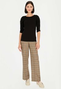 Czarny dopasowany top z marszczonymi rękawami do łokci, zestawiony z brązowymi spodniami w kratę o szerokich nogawkach i jasnymi mokasynami.