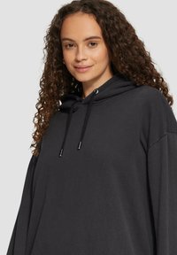 Czarny hoodie, oversize, miękka tekstura, kaptur ze sznurkiem i metalowymi akcentami, szerokie rękawy oraz swobodny styl.