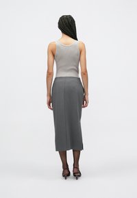 Γκρι ριμπ τοπ χωρίς μανίκια σε συνδυασμό με γκρι midi φούστα με λείο ύφασμα και πλαϊνές σχισμές, συνοδευόμενα από ψηλοτάκουνες γόβες. Μαλλιά πλεξούδα, ουδέτερο φόντο.