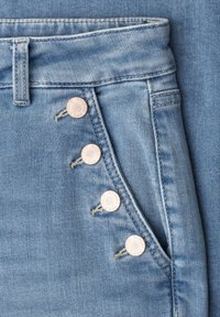 Jean en denim bleu clair avec quatre boutons en cuivre à côté d'une poche avant et une boucle de ceinture au-dessus de la taille.