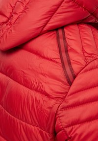 Veste doudoune rouge avec un design matelassé, mettant en valeur une texture brillante, des coutures horizontales et une bande rouge foncé contrastante le long de la poche zippée.