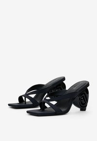 Schwarze Absatzsandalen verfügen über kreuzweise Riemen und einen einzigartigen kreisförmigen Absatz. Aus glattem Leder mit einem flachen, quadratischen Zehendesign.