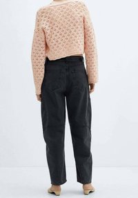 Růžový pletený zkrácený svetr s otevřeným vzorem, spárovaný s volnými tmavě šedými džíny s bočními kapsami.