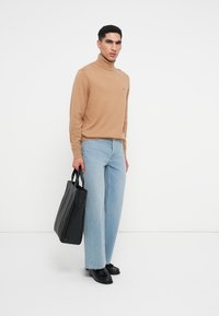 Beige turtleneck-sweater, vaaleansiniset leveät farkut, mustat nahkakengät ja jäykkä musta käsilaukku. Yksinkertainen muotoilu, sileä tekstuuri.