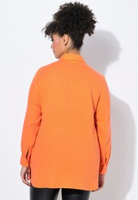 Camicia a maniche lunghe arancione con un tessuto strutturato e stropicciato. Caratterizzata da un colletto, polsini con bottoni e una vestibilità comoda, che arriva a metà fianchi.